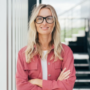 Frau mit langen blonden haaren, hat die Arme verschränkt und lächelt in die Kamera